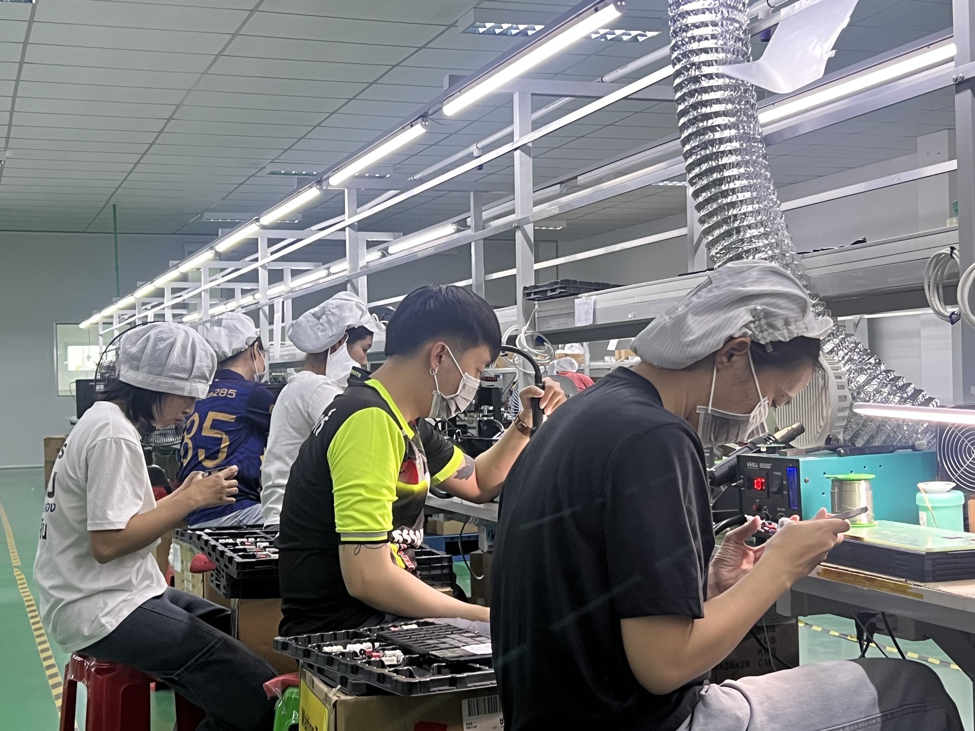 Wide view of 5-station manual assembly line with white-coated workers